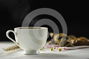 Hot coffee in white cup, with smoke and bakery placed on white wood table, dark background With sunshine in morning,Beauty concept