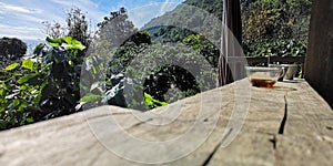 Hot coffee on a wooden floor with sunshine and mountains as background