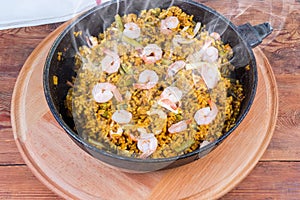 Hot cooked seafood paella in pan on wooden serving board