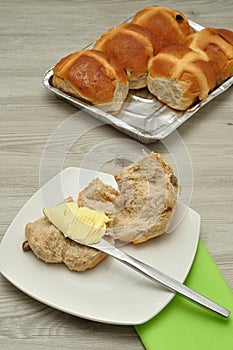 Hot cross buns, butter, knife and green napkin