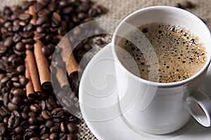 hot cup of coffee with cinnamon and coffee grains