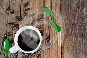 Hot cup of coffee with smoke, coffee beans and green leaves on vintage wooden background