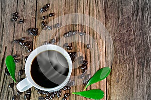 Hot cup of coffee with smoke, coffee beans and leaves on vintage grunge wooden background