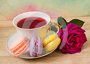 Hot cup of tea, colored cakes and pink flower