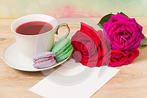 Hot cup of tea, colored cakes and pink flower
