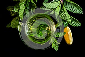 Hot cup of tea with fresh mint leaf and lemon on black background