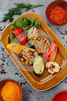 Hot delicious grilled vegetables on a brown ceramic plate on a grey background