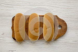 Hot dog buns on wooden board on white wooden background, top view. Flat lay, from above, overhead.
