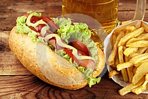 Hot dog with glass of beer with french fries on wooden board photo