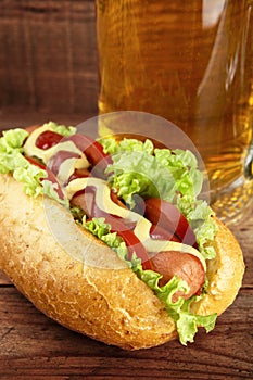 Hot dog with glass of beer on wooden board photo