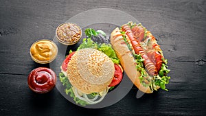 Hot dog and hamburger with cheese, meat and greens on Wooden background.