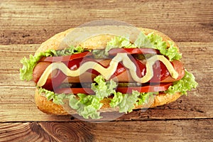 Hot dog with lettuce, tomatoes and cucumber on wooden board