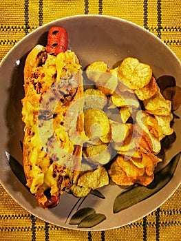 Hot dog with melted cheese topping and accompanying potato chips. photo