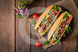 Hot dog with pickles, tomato and lettuce on wooden background.