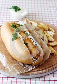 Hot dog with sausage and salad, served with french fries, mustard and mayonnaise sauce. Rustic style, selective focus.