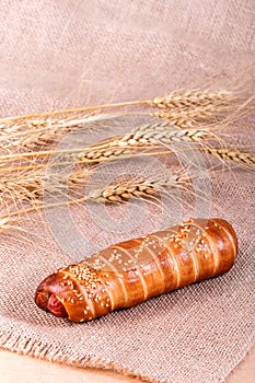 Hot dog with sesame seeds on rustic background with spikelets
