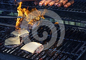 Hot dogs and cheeseburgers being grilled with flames covering one