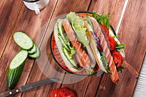 Hot dogs with cucumber lettuce and tomatoes on top of a wooden table