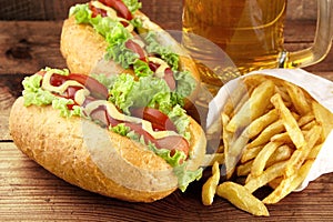 Hot dogs with glass of beer with french fries on wooden board photo