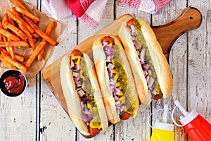 Hot dogs with onions, relish, mustard and ketchup served with french fries over white wood