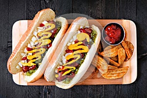 Hot dogs and potato wedges on wooden board, overhead view