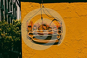 Hot dogs trendy LED sign against yellow wall. Fast food bistro, cafe exterior.