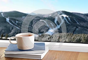 Hot drink and books near window with view of mountain landscape