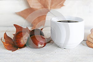 Hot drink, cup of coffee in a traditional Catalan Halloween party castanyada. Three chestnuts on a leaf and white wooden table. photo