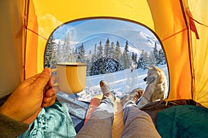 Hot drink in the hand and wonderful view of snowy forest through the open entrance to the tent. The beauty of a romantic hike and