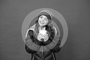 Hot drink for winter morning. Small girl hold tea cup red background. Happy child with winter look. Hot chocolate