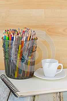 Hot Espresso coffee cup next to coloring colored pencils on sketch drawing book. .