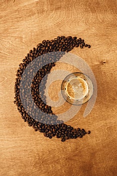 Hot espresso with foam in glass cup and aromatic roasted coffee beans in shape of moon on wooden table. Flat lay, Copy space.