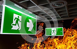 Hot flame fire and green fire escape sign hang on the ceiling in the office at night. The concept of fire escape training and