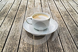 Hot foaming cappuccino in a white ceramic cup on a saucer stands on a table of wooden boards photo