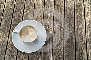 Hot foaming cappuccino in a white ceramic cup on a saucer stands on a table of wooden boards with space for writing photo