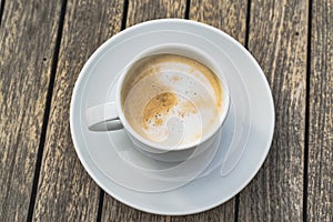 Hot foaming cappuccino in a white ceramich cup on a saucer stands on a wooden table, top view photo