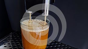 Hot fragrant black coffee with high foam is poured from the coffee machine into a transparent glass.