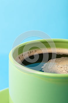 Hot fresh coffee with foam in the green cup on a color background