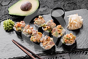 Hot fried Sushi rolls and maki set with smoked eel, cream cheese, avocado, caviar and wasabi on black slate background.