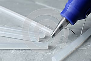 Hot glue gun and sticks on light grey marble table, closeup