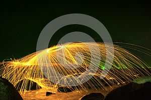 Hot Golden Sparks Flying from Man Spinning Burning Steel Wool into a Sphere on a Rocky Shoreline.