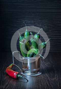 Hot green peppers in a metal cup holder stand on a table