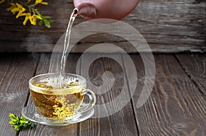 Hot green tea is poured from the teapot into the glass bowl, vintage wooden table, steam rises above the cup. Tea leaves next to