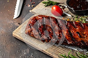 hot grilled spare ribs on cutting board on a dark background. American Spare Ribs in BBQ Sauce. Restaurant menu, dieting, cookbook