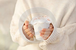 Hot hands holding a white mug with cream topping