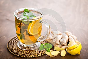 Hot herbal tea with fresh lemon, ginger and mint leaves on brown background,