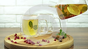 Hot herbal tea with red crandberries poured into glass cup from glass teapot. White background
