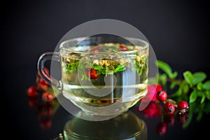 Hot herbal tea from various herbs in glass cup on black background