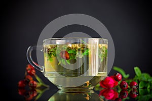 Hot herbal tea from various herbs in glass cup on black background
