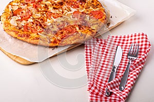 Hot homemade pizza with chicken meat, tomatoes, onions near with cutlery fork and knife on red tablecloth, angle view